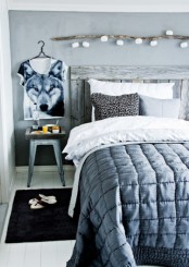 a monochromatic Scandinavian bedroom with a reclaimed wood bed, grey and white bedding, a branch over the bed with string lights