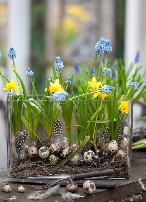 a creative spring decoration - a large glass vase with hay, fake eggs and feathers and blue hyacinths and yellow daffodils