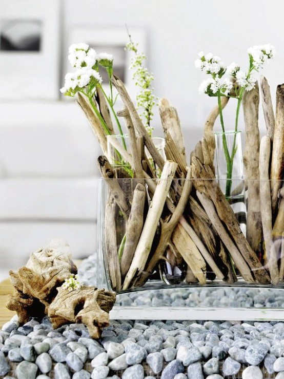 a glass jar with driftwood and greenery plus some blooms for a centerpiece