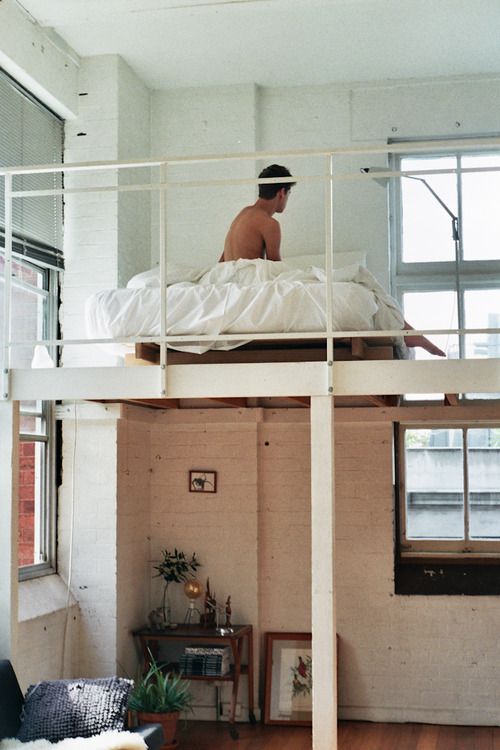 a loft bedroom with a large bed and neutral bedding, with windows that flood the space with light