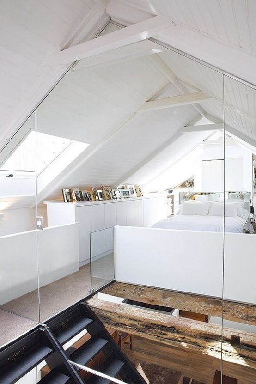 a white loft bedroom with skylights, a white bed with neutral bedding, a cabinet with books on top is an airy and lovely space to sleep in