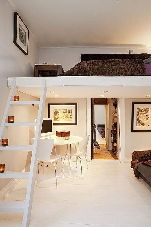 a small neutral space with a ladder up and a loft bedroom, a bed with dark bedidng and a low dark-stained coffee table