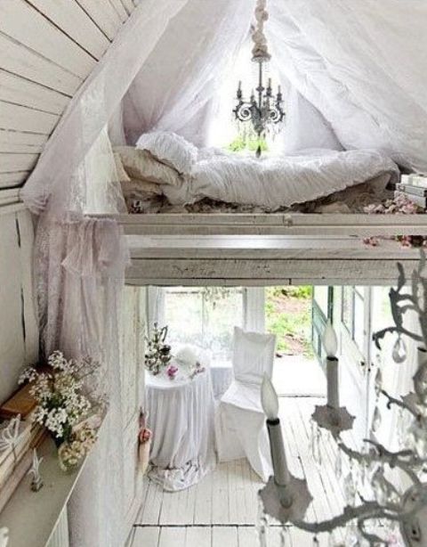 a neutral shabby chic space with a tiny loft bedroom, a skylight with curtains, a comfy bed and a lovely chandelier
