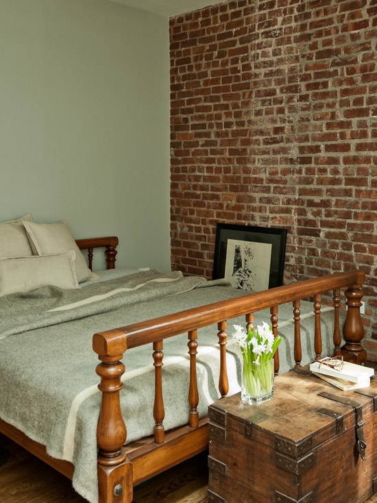 a small vintage-inspired bedroom with wooden furniture and a red brick statement wall that adds texture and a bright shade to the space