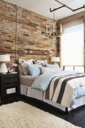 a chic bedroom with art deco touches and a fake brick wall that brings texture along with pipes and antlers