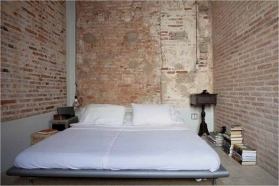 a very simple bedroom with a laconic modern bed and exposed brick walls aorund that add color, texture and interest taking over the whole space