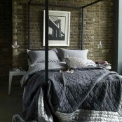 a moody bedroom with a dark brick statement wall and a black canopy bed looks very chic and welcoming