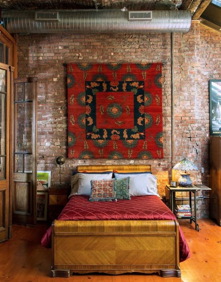 an industrial bedroom with a brick wall, an exposed pipe, metal furniture is softened with a stylish bed and a boho rug