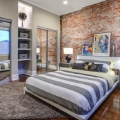 a traditional bedroom is spruced up with a red brick statement wall and rich stained wood floors