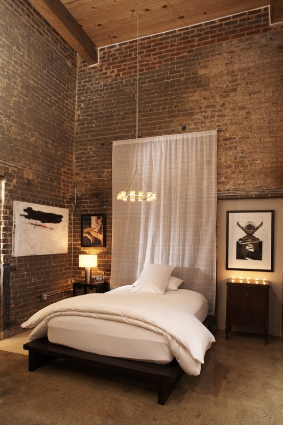 exposed brick double height walls are softened with an airy curtain, chic lamps and a stylish bed
