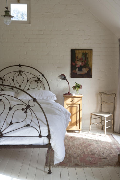 an airy girlish bedroom with a white brick wall and a forged bed, shabby chic and vintage furniture
