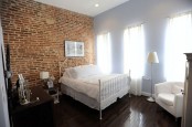 a red rick wall and dark floors are softened with an ethereal forged bed and airy curtains