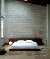 a sleek contemporary bedroom with grey brick walls, a livign edge wooden bed and faux animal skins on the floor