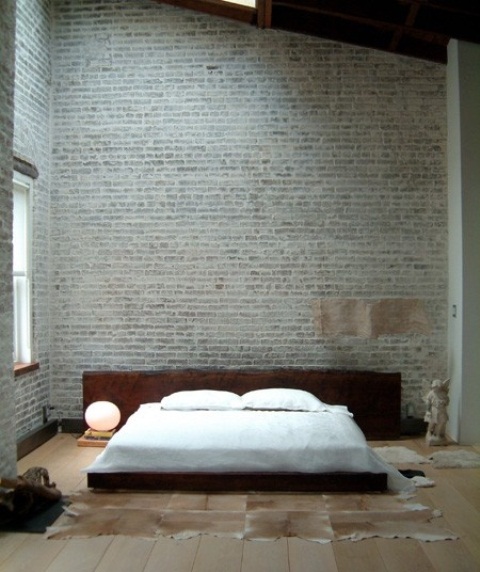 a sleek contemporary bedroom with grey brick walls, a livign edge wooden bed and faux animal skins on the floor