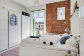 a white Scandinavian bedroom is refreshed with a single exposed brick wall that adds color and texture