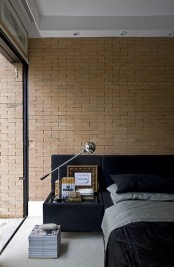 a contemporary bedroom with a faux brick wall of a sandy shade and a velvet upholstered black bed