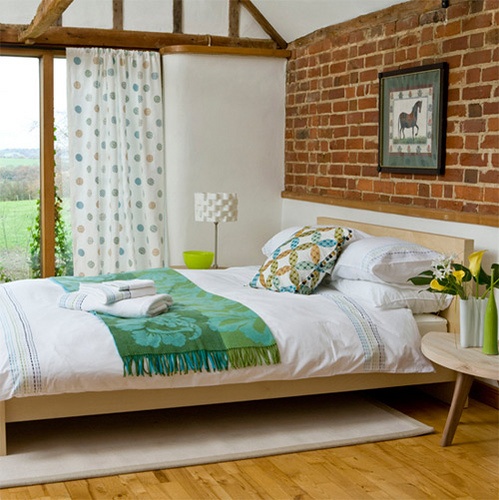 a mid-century modern inspired bedroom with colorful textiles and prints and an exposed brick wall and wooden beams for more texture