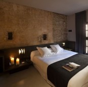 a stone and brick wall brings more interest to the space and a black upholstered bed contrasts it