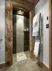 a modern chalet bathroom clad with tiles, with concrete and light-stained rough wood framing the shower space