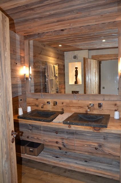 a modern rich-stained bathroom clad with wood, with a large mirror, a double vanity with open shelves and lights