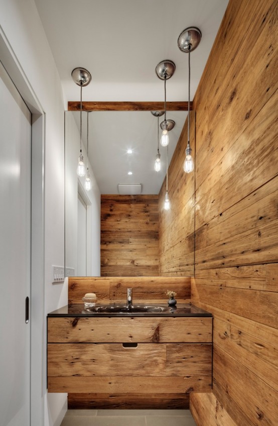 a modern bathroom with a chalet feel - a light-stained wooden wall, a matching built-in vanity, a large mirror and bulbs hanging down