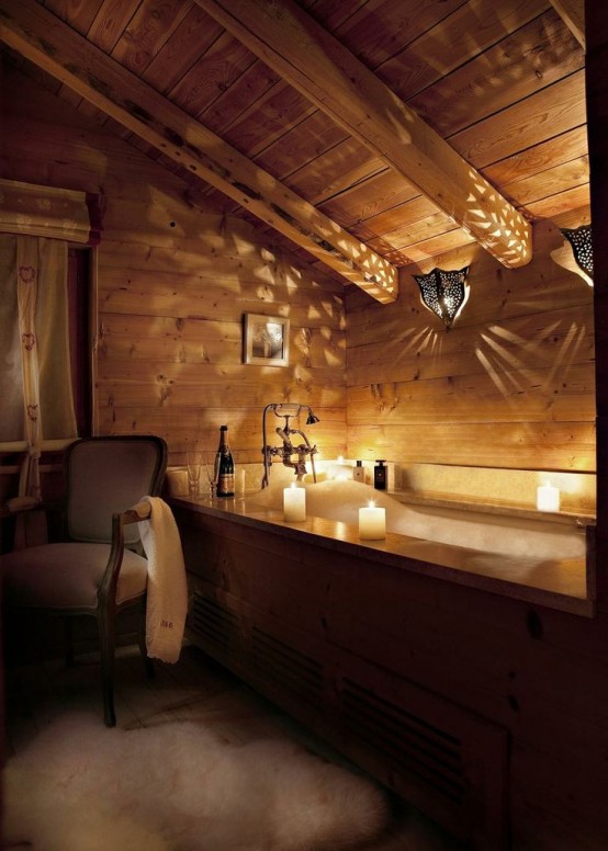 a beautiful chalet bathroom clad with wood, with a bathtub clad with wood, a vintage chair and a faux fur rug plus lights
