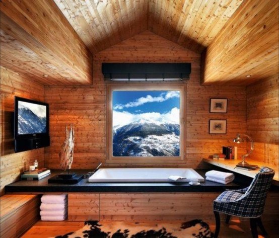 a stylish and cool chalet bathroom clad with light-stained wood, with a view, a TV, a chair, towels, lamps and a blanket