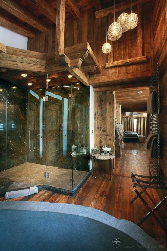 a large chalet bathroom clad with rich-stained wood, with windows, a large glass-enclosed shower and lamps