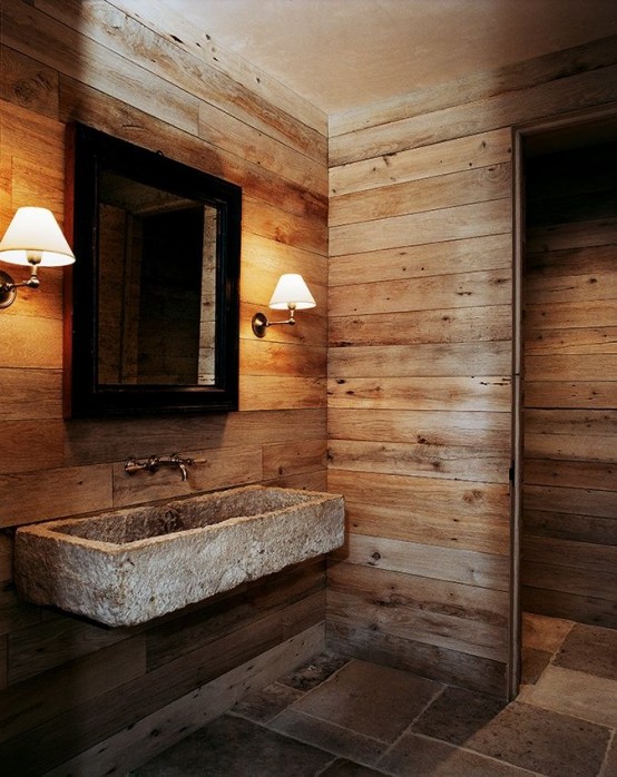 a wabi-sabi chalet bathroom clad with aged wood, a stone floor and a stone wall-mounted sink plus sconces