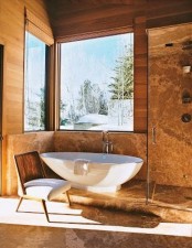 a chalet bathroom clad with light-stained wood and stone, with windows for a view, an oval tub and a glass-enclosed shower space