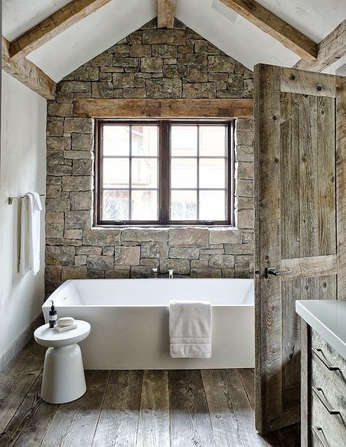 a chalet bathroom with a stone clad accent wall, a bathtub and a stool, a window with a mountain view and aged wood everywhere