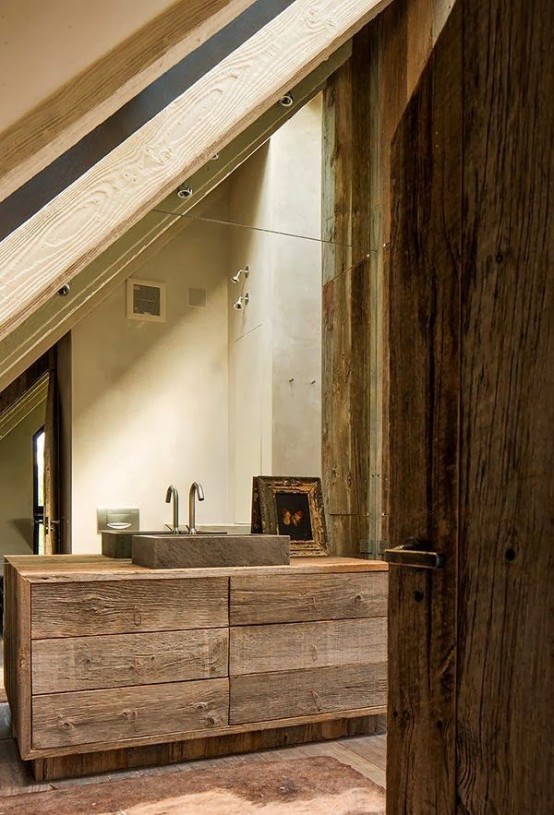 a chalet bathroom clad with reclaimed wood, with an aged wood vanity, a stone sink and a large mirror covering the whole wall