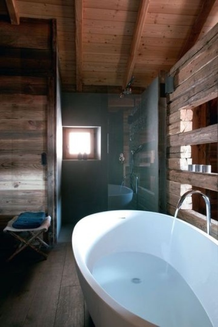 a modern chalet bathroom fully clad with reclaimed wood, with some windows for natural light and an oval free-standing tub