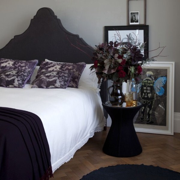 a modern bedroom with a touch of Gothic, a refined black upholstered bed, a black nightstand, catchy artworks and a moody floral arrangement