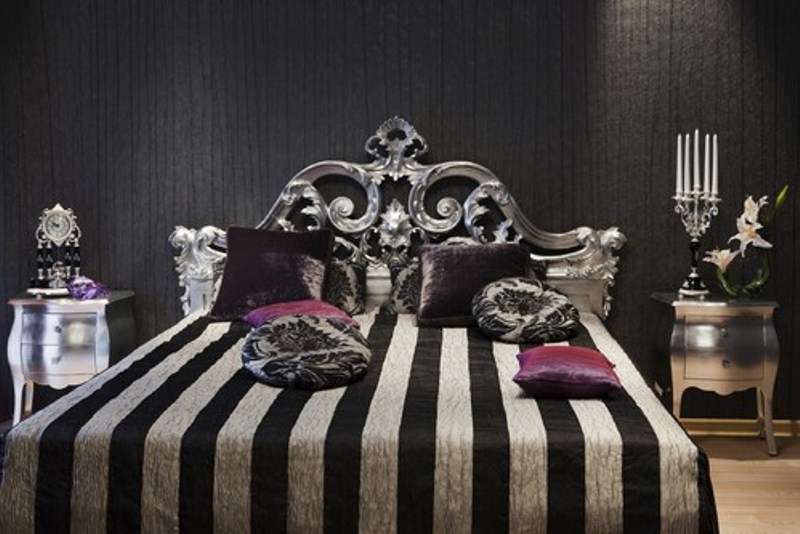 a catchy modern Gothic bedroom with a black textural wall, a refined metallic bed, shiny nightstands and bold bedding, striped and purple
