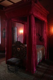 a vintage Gothic bedroom done in crimson, with printed wallpaper, a canopy bed in a matching color and exquisite furniture