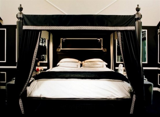 a Gothic-infused bedroom with black and white walls, a matching canopy bed, printed bedding, matching mirrors on both sides of the bed