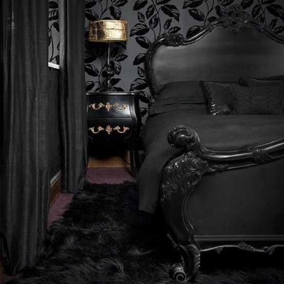 a refined Gothic bedroom with black botanical wallpaper, a sophisticated black bed, black and gold nightstands, a gold lamp and black textiles