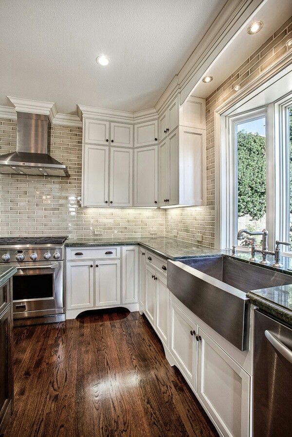 a vintage farmhouse kitchen with white cabinetry, a whitewashed red brick backsplash and stainless steel appliances