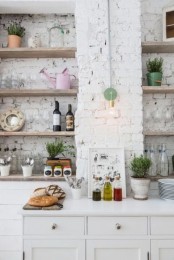 a contemporary Scandinavian kitchen with whitewashed brick walls, white cabinetry, open shelves, lamps and greenery is cool