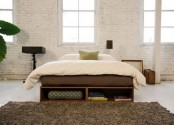 a modern bedroom with whitewashed brick walls, a modern bed with storage, lamps right on the floor and a fluffy rug