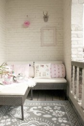 a balcony with whitewashed brick walls, a small sectional rattan sofa and printed pillows