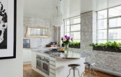 an elegant kitchen with whitewashed brick walls, modern white cabinetry, steel countertops and stools plus a crystal chandelier