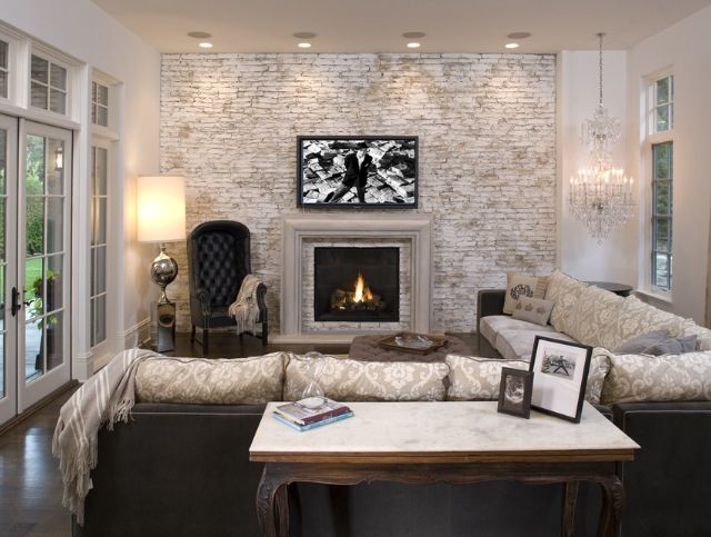 a vintage living room with a whitewashed brick wall, a fireplace, a crystal chandelier, a large corner sofa, a refined chair and lights