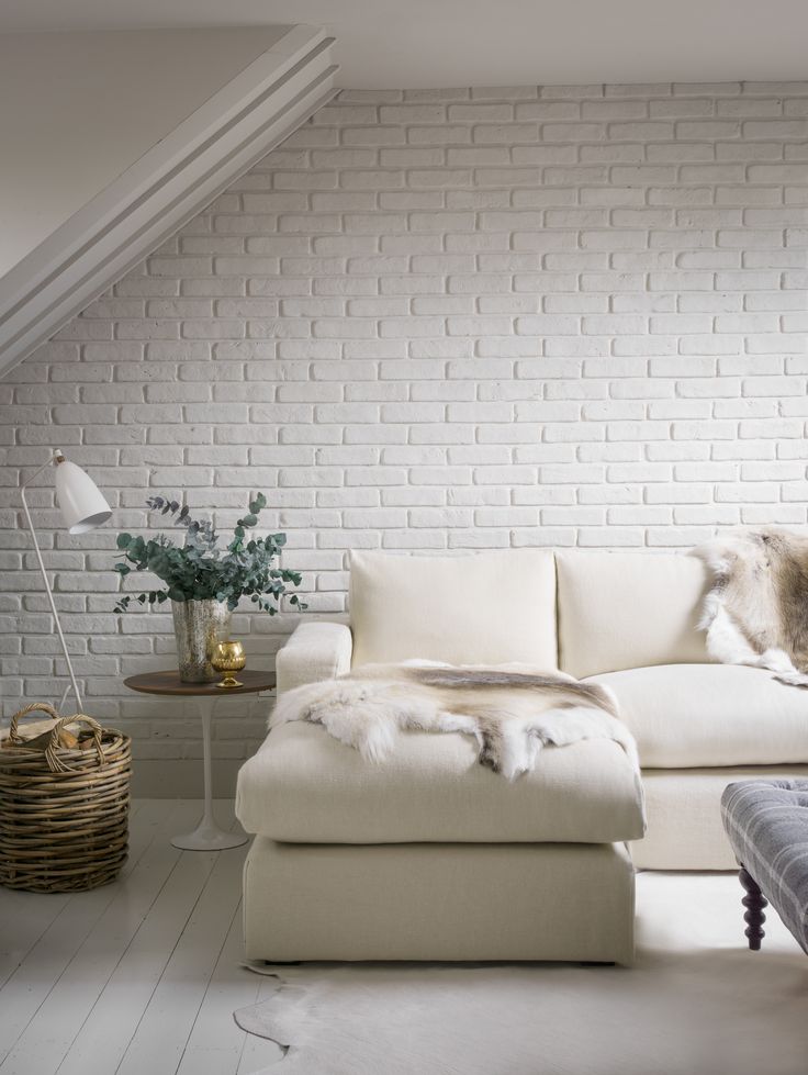 a modern neutral living room with a faux whitewashed brick wall, a corner sofa, a table and a baket is very welcoming