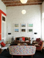 a mid-century modern living room with whitewashed brick walls, elegant sofas and chairs, a chic gallery wall, bright and printed pillows and pendant lamps