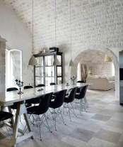 a beautiful dining space with whitewashed brick walls and a ceiling, a trestle table, black chairs and pendant lamps over the table