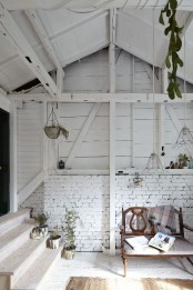 a refined entryway done with whitewashed wooden and brick walls, refined furniture and potted greenery plus pendant lamps