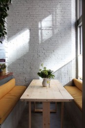 a contemporary dining space with a whitewashed brick wall, upholstered benches and a wooden table is very welcoming and light-filled