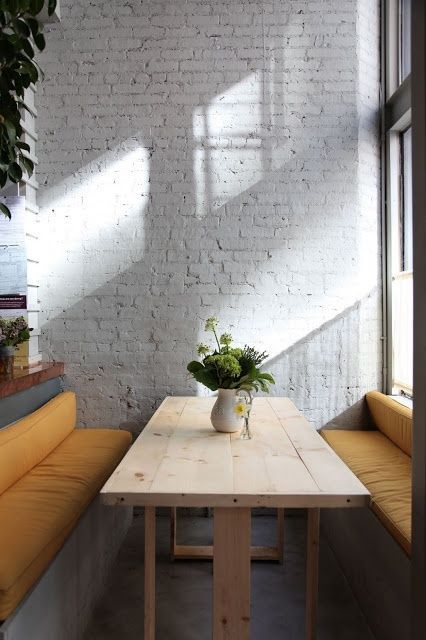 a contemporary dining space with a whitewashed brick wall, upholstered benches and a wooden table is very welcoming and light filled